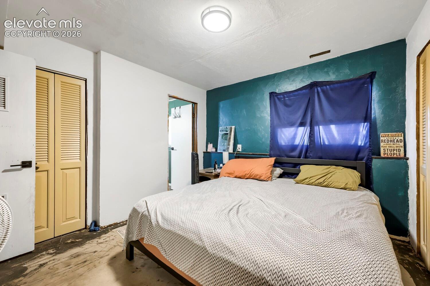 Room featuring a window, built-in closet with louvered doors, and a ceiling-mounted light fixture