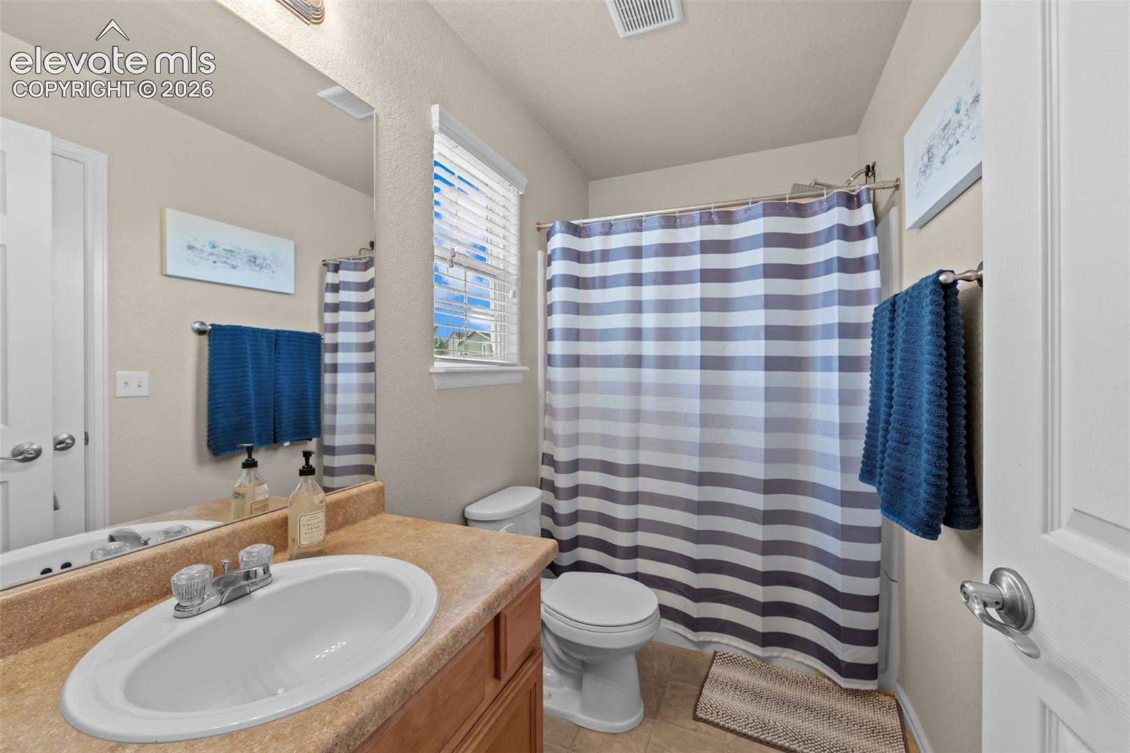 Bathroom featuring a single vanity with an integrated sink, a built-in mirror, a toilet, a shower/tub combination, and a window with blinds