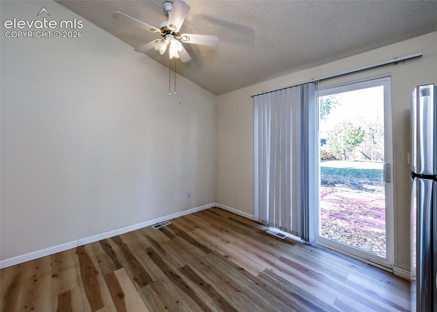 Wood-finish flooring, vaulted ceiling, stainless steel refrigerator, and glass sliding door featuring vertical blinds