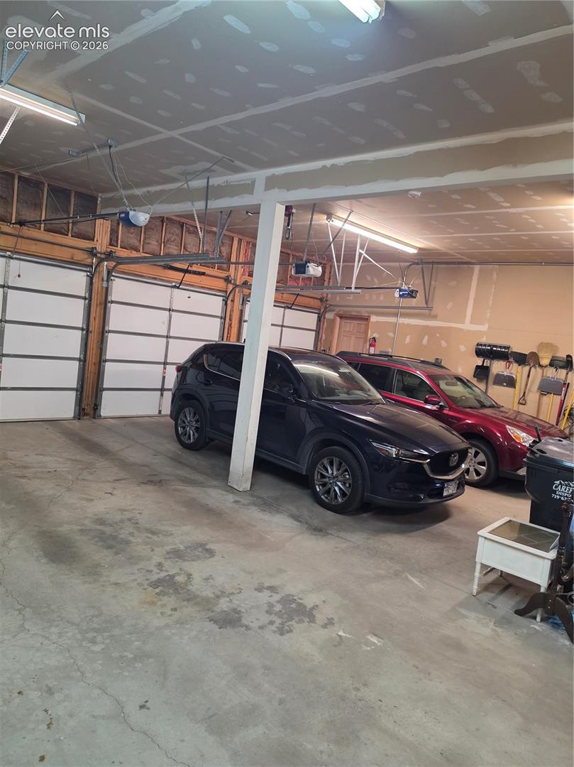 Three overhead garage doors with automatic openers, concrete flooring, and fluorescent ceiling lighting