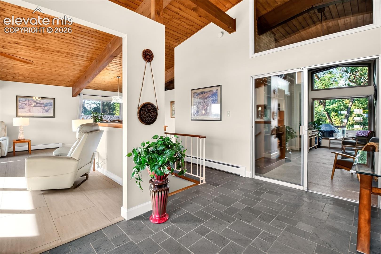 The open floor plan includes slate flooring in the entry and shows the wood ceilings and provdes a peak into the sunroom area.