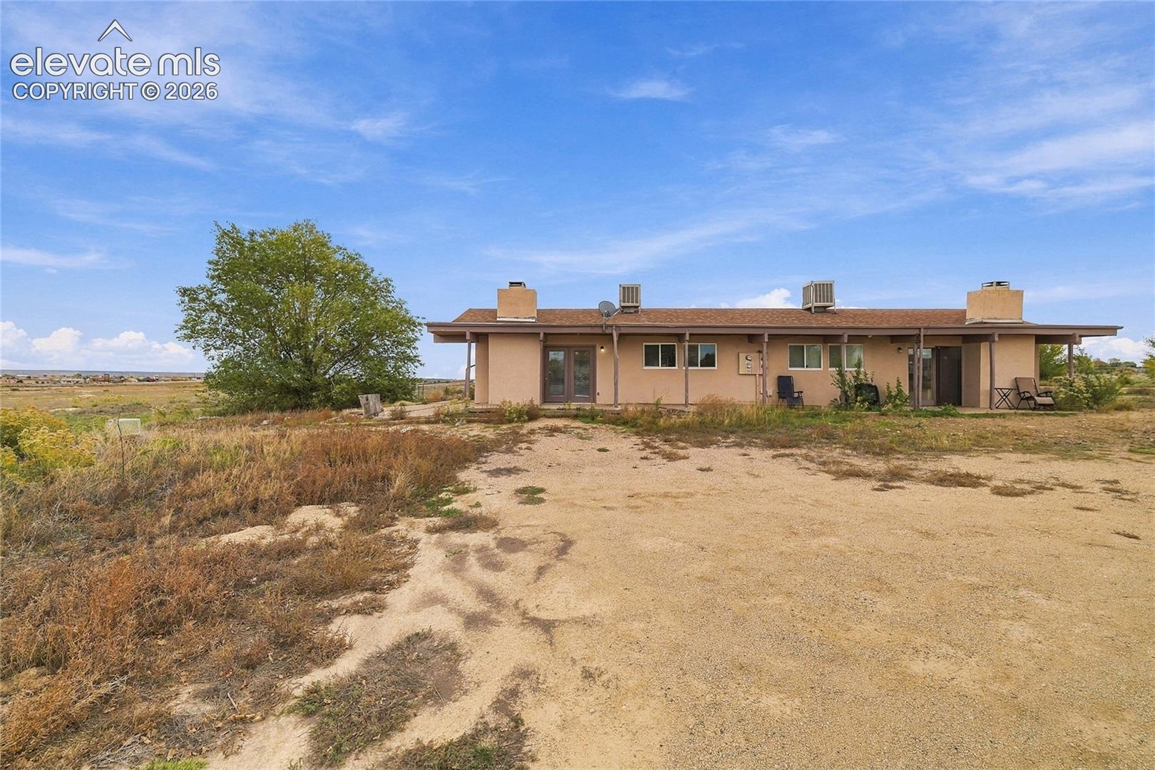 Single-story exterior featuring a low-pitch roof, dual exterior chimneys, a full-length covered patio, and expansive desert acreage