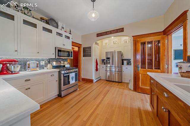 Kitchen with appliances with stainless steel finishes, tasteful backsplash, light countertops, arched walkways, and light wood-style flooring