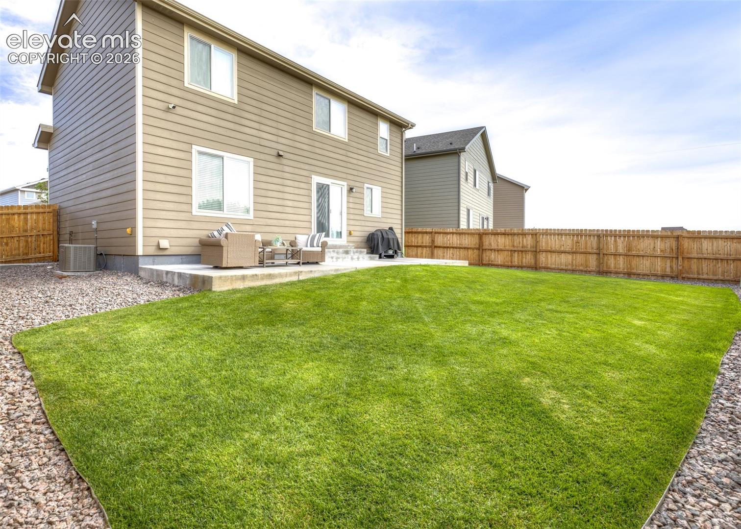 Exterior of home featuring horizontal siding, a concrete patio, and a fully fenced backyard with a grass lawn and stone ground cover