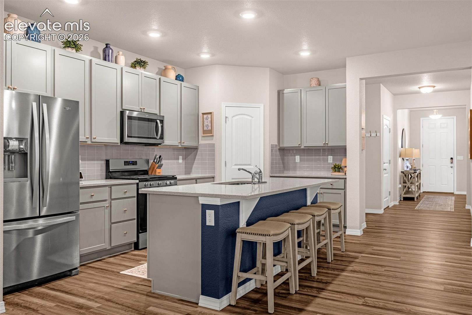 Kitchen featuring light gray cabinetry, stainless steel appliances, a center island with seating, recessed lighting, and wood-finish flooring