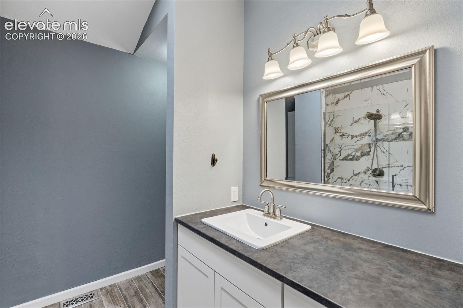 Single vanity with a white rectangular sink, brushed nickel faucet, dark countertop, and white cabinetry