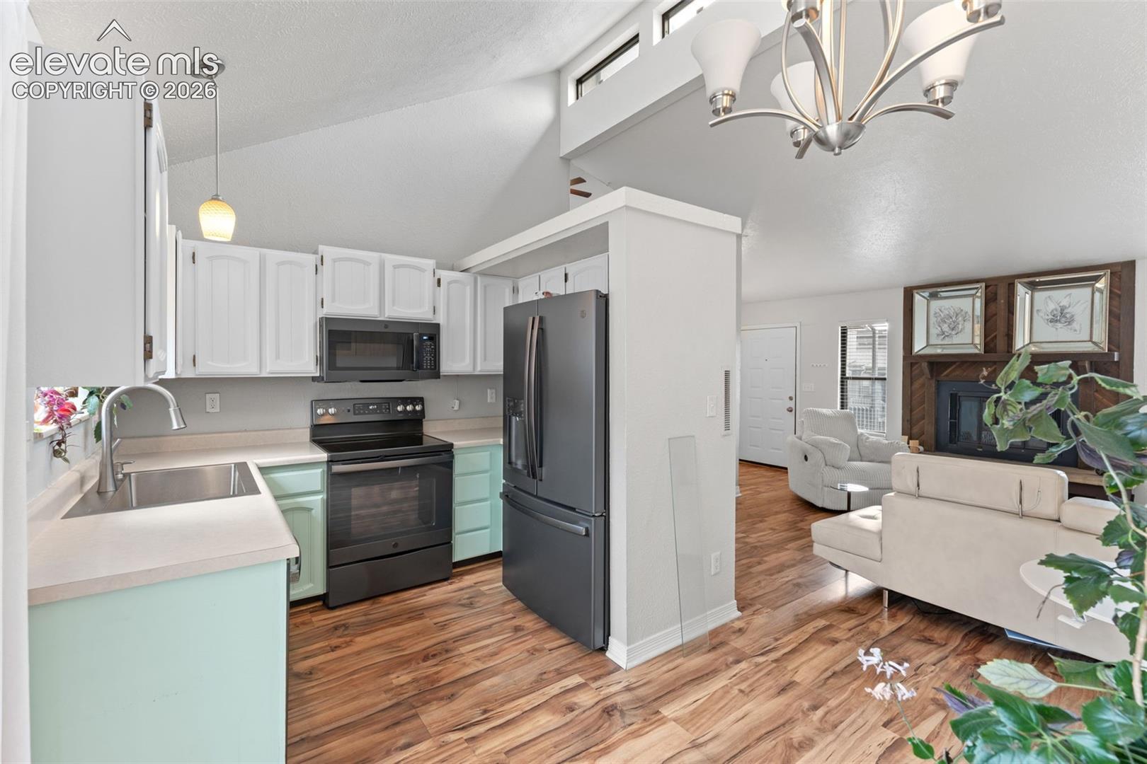 Vaulted ceilings with clerestory windows, wood-finish flooring, a kitchen featuring light cabinetry and dark appliances, and a fireplace with a wood surround