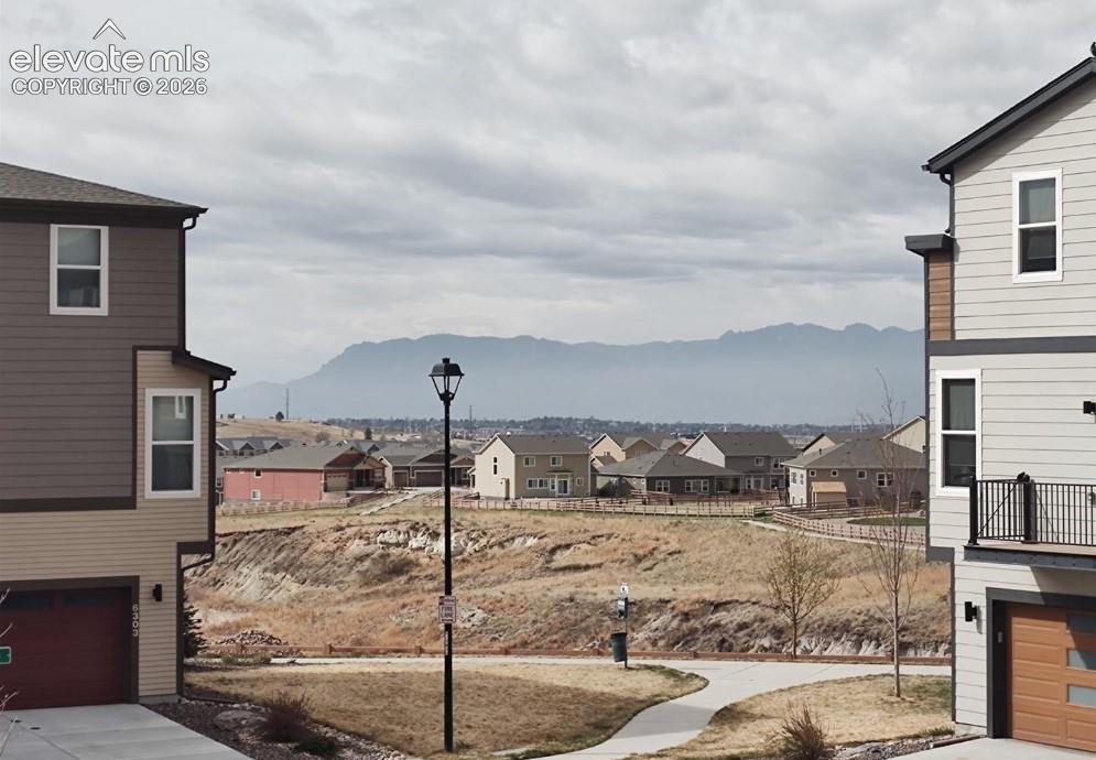Multi-story residences featuring horizontal siding, integrated garages with roll-up doors, and metal railings, highlighted by a backdrop of mountain scenery