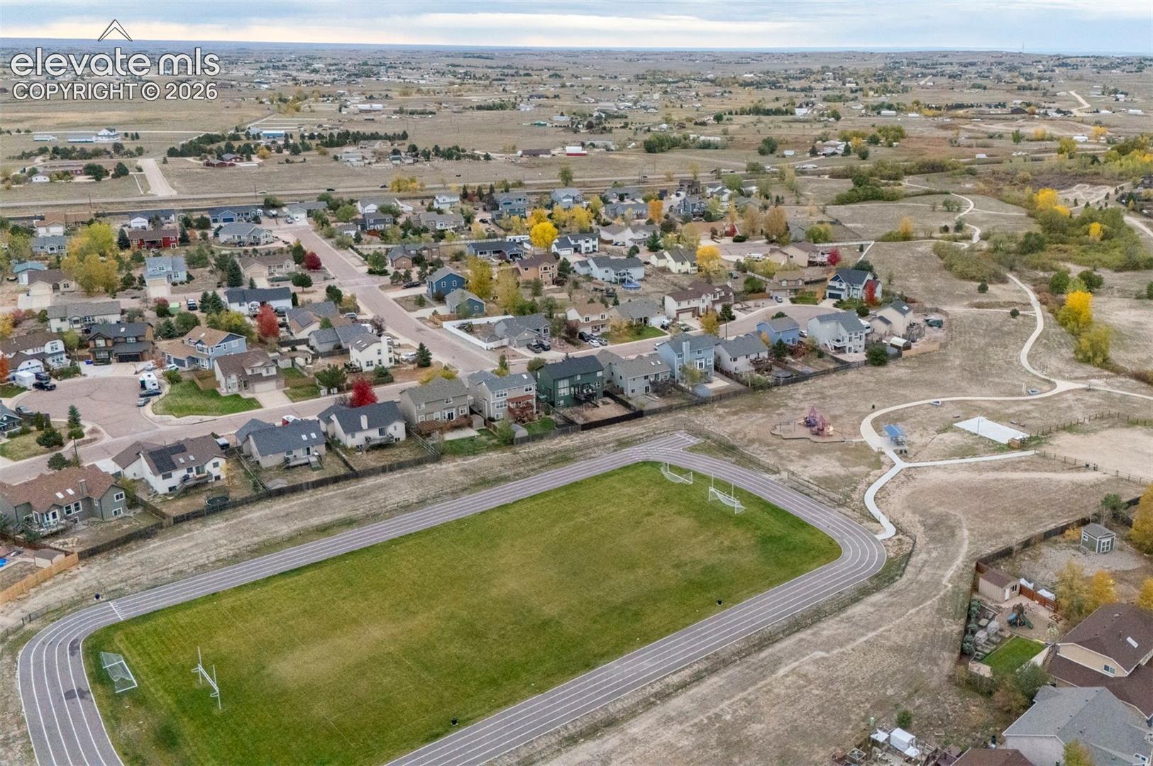Aerial perspective featuring an expansive turf field, a paved running track, integrated goal posts, and adjacent walking paths