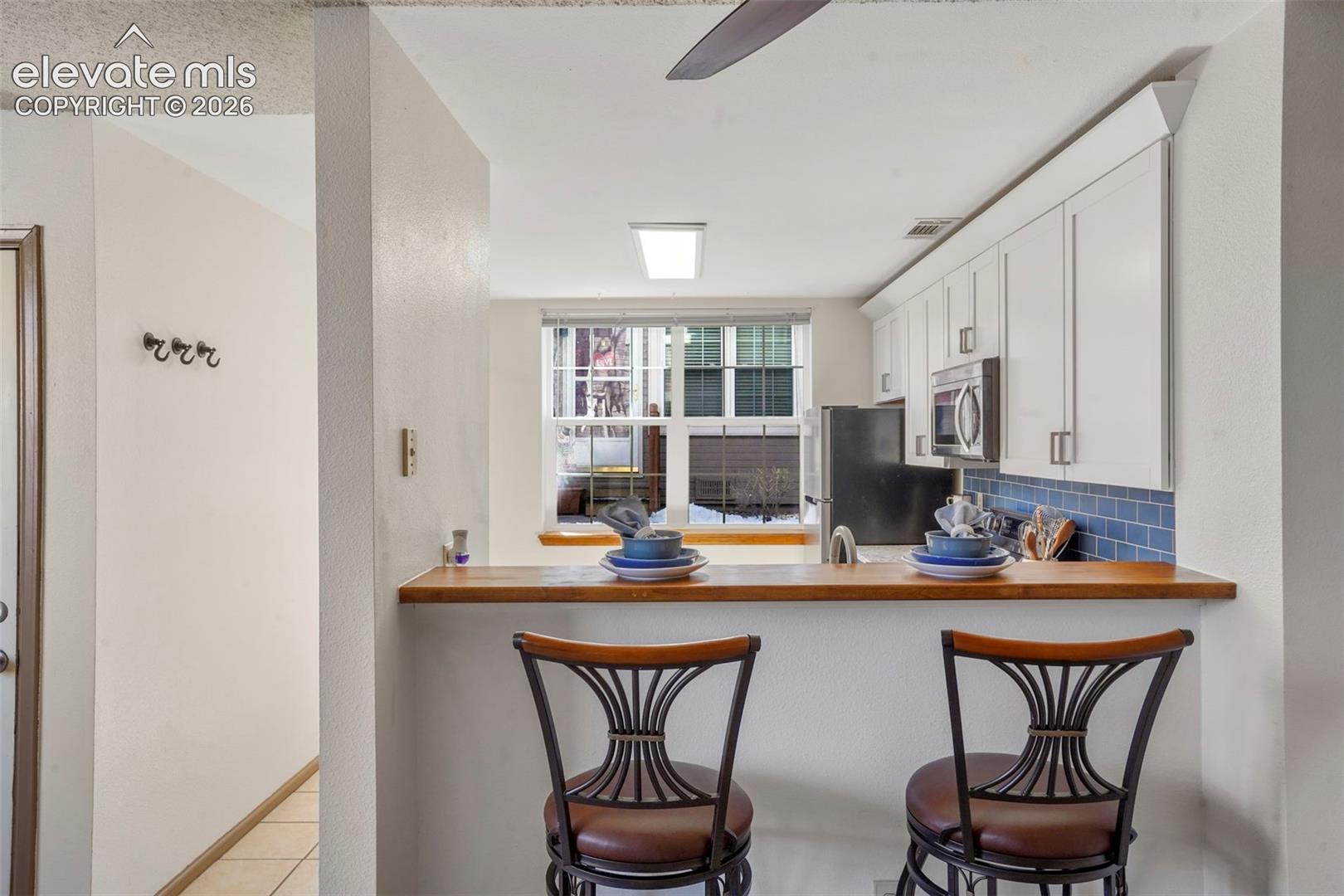 Kitchen with white cabinetry, a kitchen bar, backsplash, appliances with stainless steel finishes, and light tile patterned floors