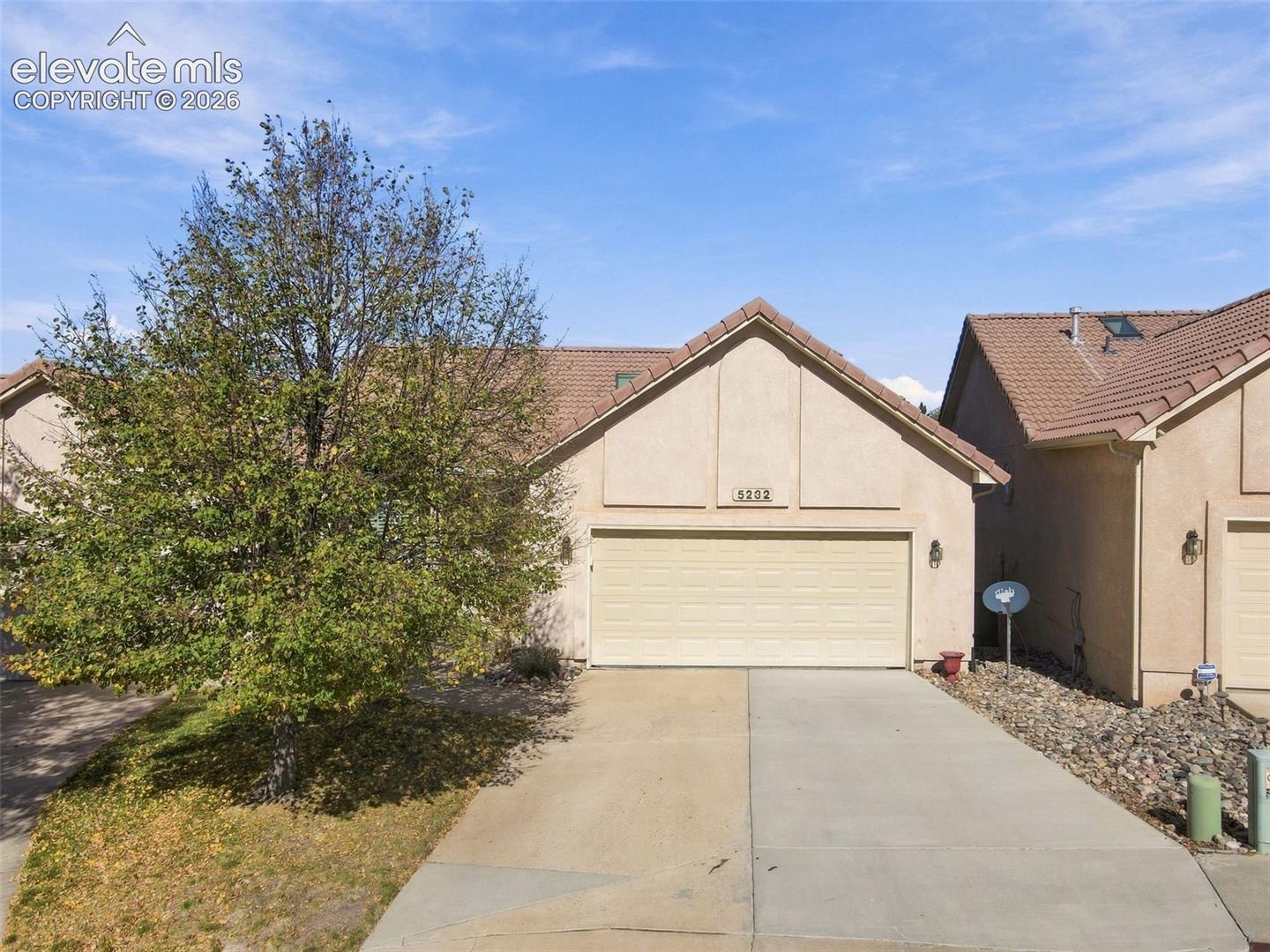 Stucco exterior residence featuring a tile roof, an attached two-car garage, concrete driveway, and mature landscaping