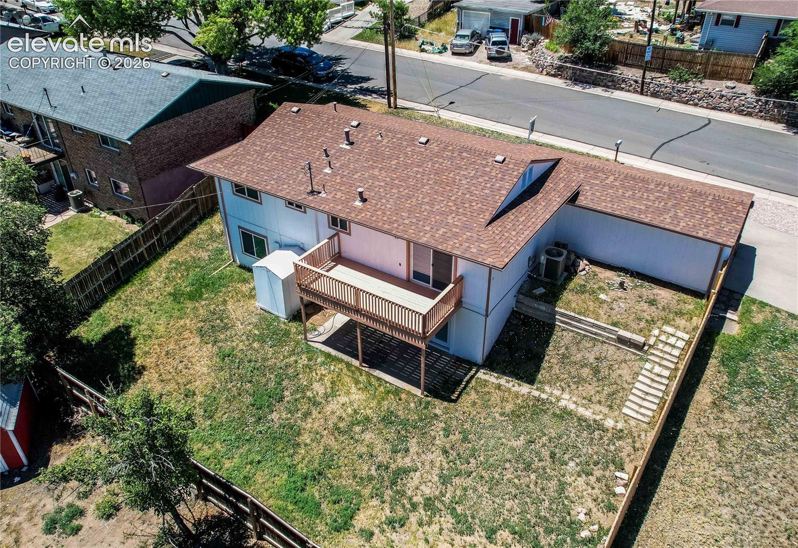 Aerial perspective of the property featuring a raised wood deck, skylight, exterior air conditioning unit, and fenced backyard with stone pavers