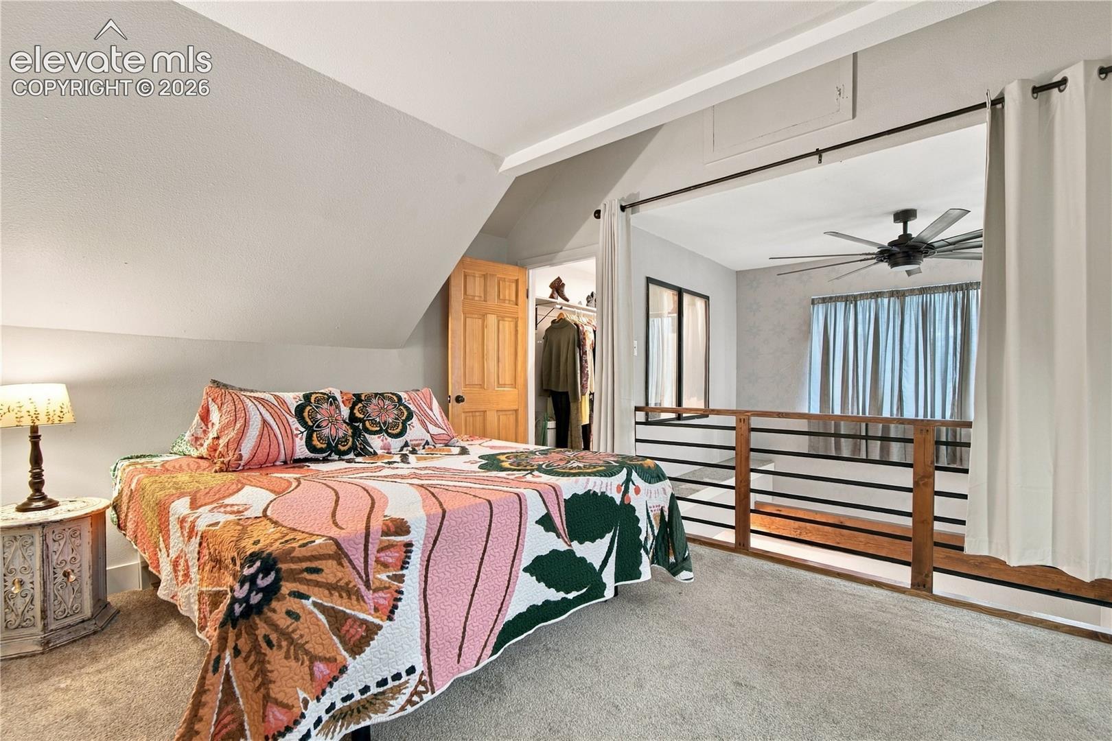 Vaulted ceilings, metal railing with horizontal bars, carpeted flooring, built-in closet, and ceiling fan