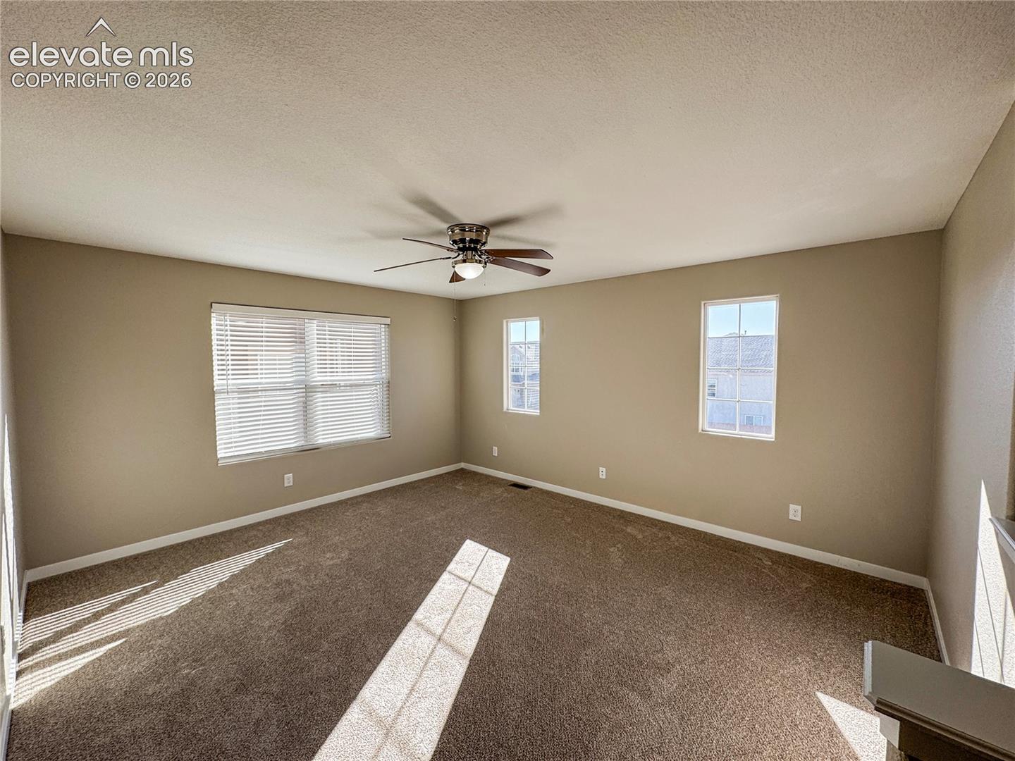 Neutral-toned interior featuring wall-to-wall carpeting, three windows with grid muntins, and a ceiling fan with integrated lighting