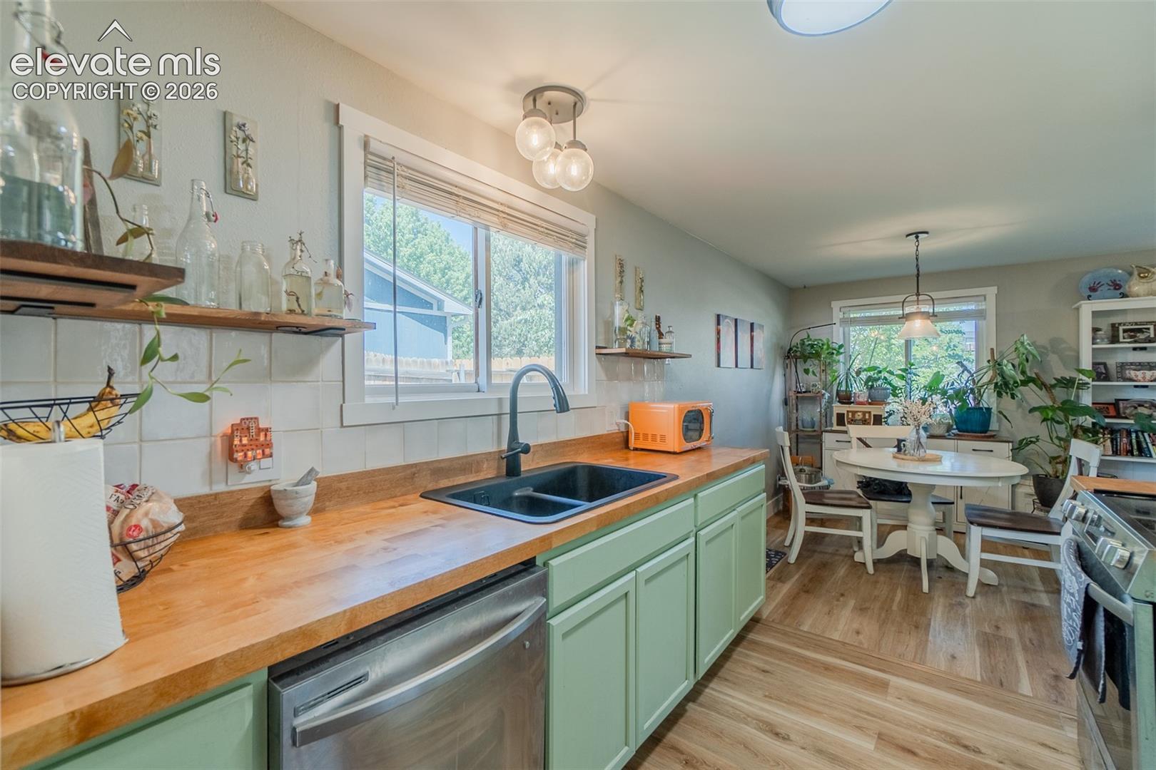 Kitchen featuring butcher block countertops, light green cabinetry, a stainless steel dishwasher, and open shelving