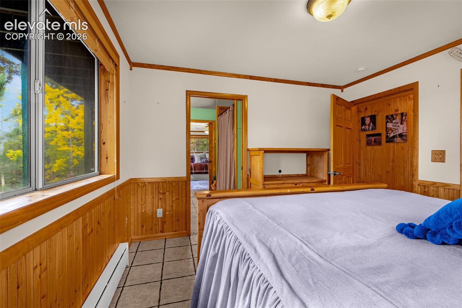Room featuring wood paneling, tile flooring, crown molding, and a multi-pane window