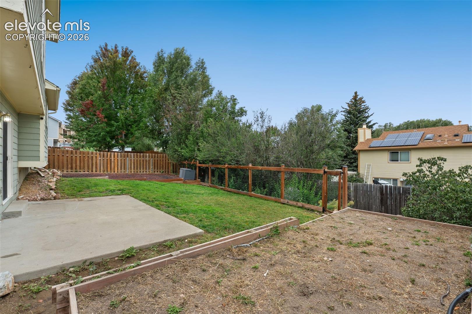 Expansive backyard featuring a concrete patio, wood fencing, and a terraced earth area