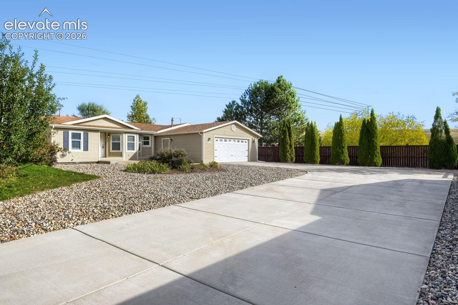 Single-story residence featuring horizontal siding, a two-car attached garage, a concrete driveway, and rock-based landscaping with perimeter privacy fencing