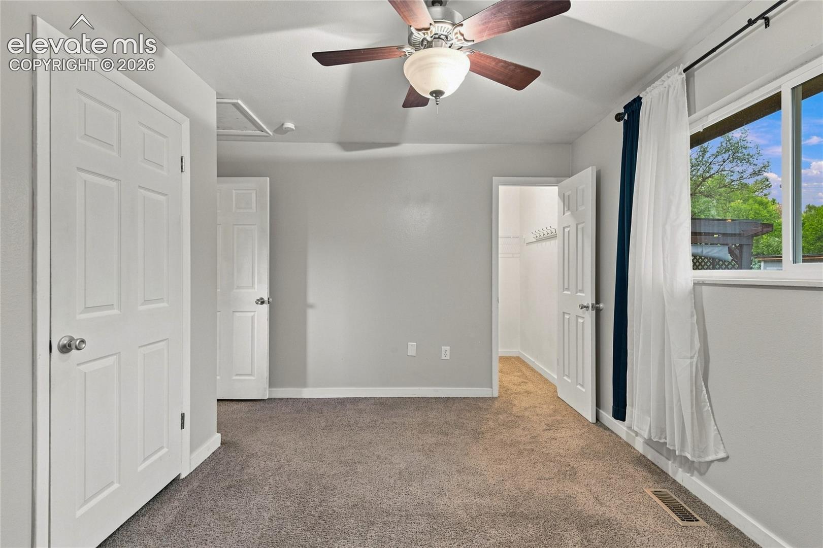 Spacious primary bedroom featuring walk-in closet, carpet flooring, a ceiling fan with integrated lighting, and large windows with dual-layer window treatments