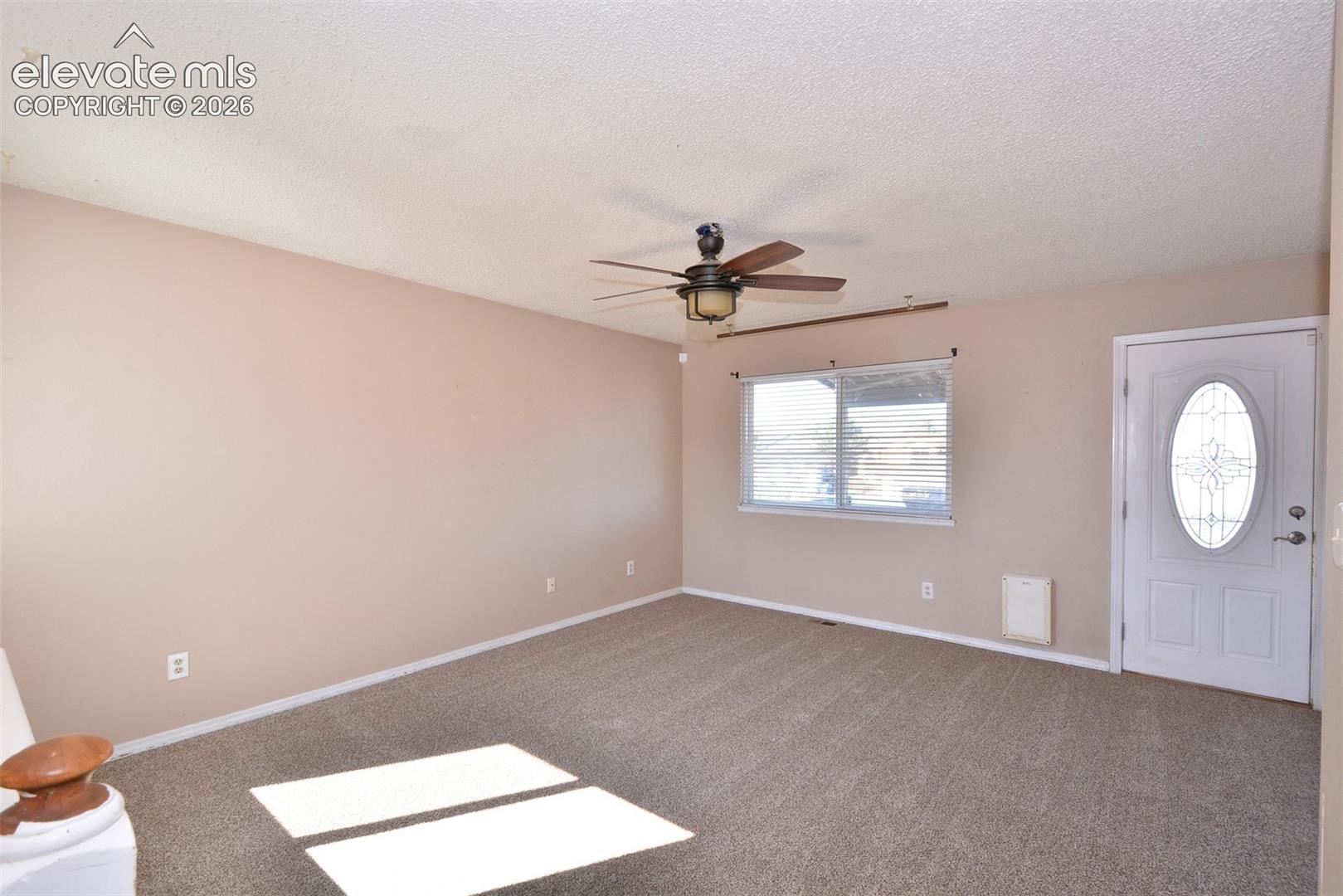 Neutral tone wall paint, carpet flooring, a ceiling fan with light fixture, and a window with blinds