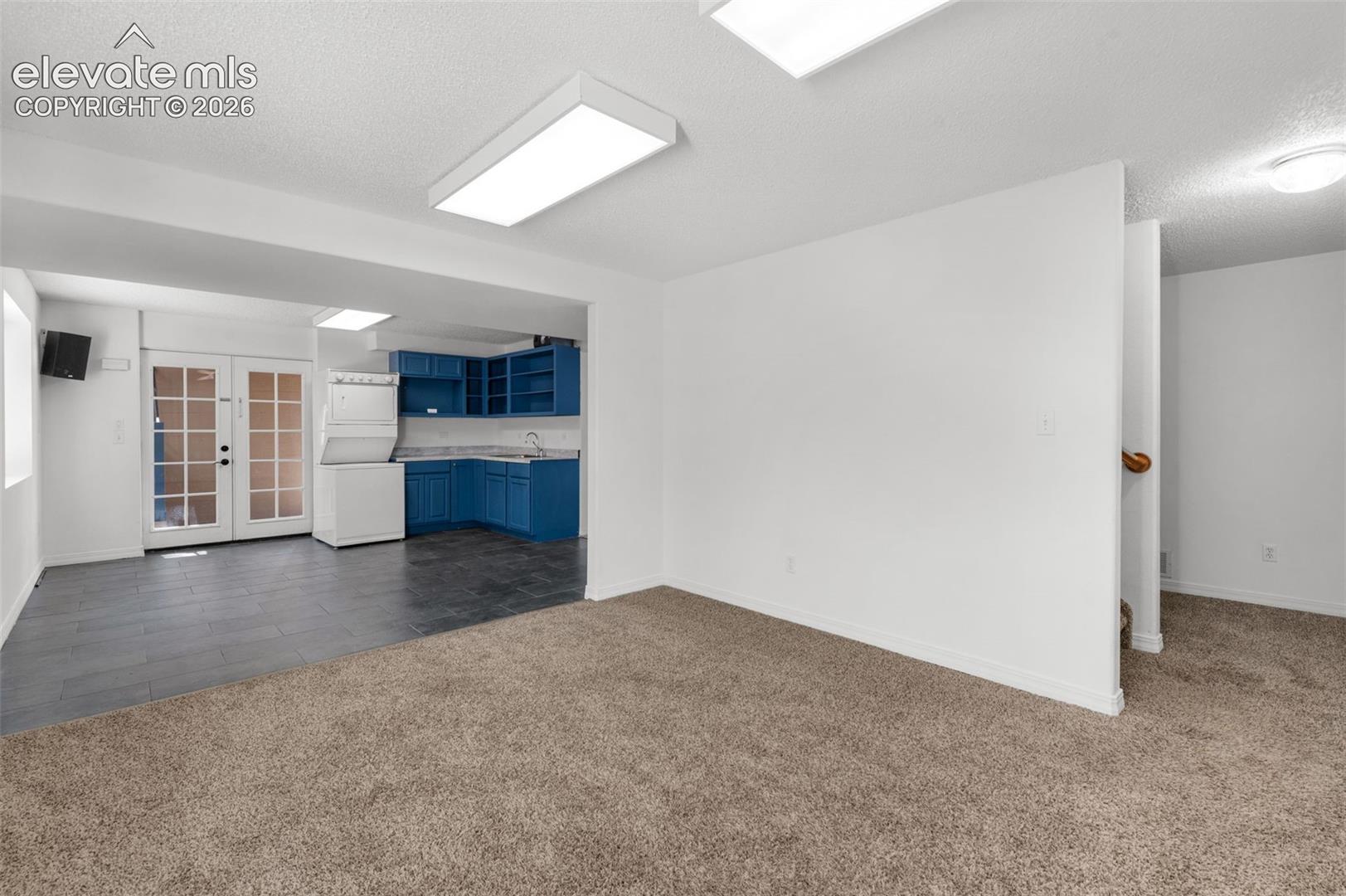 Carpeted living area with white walls and overhead lighting