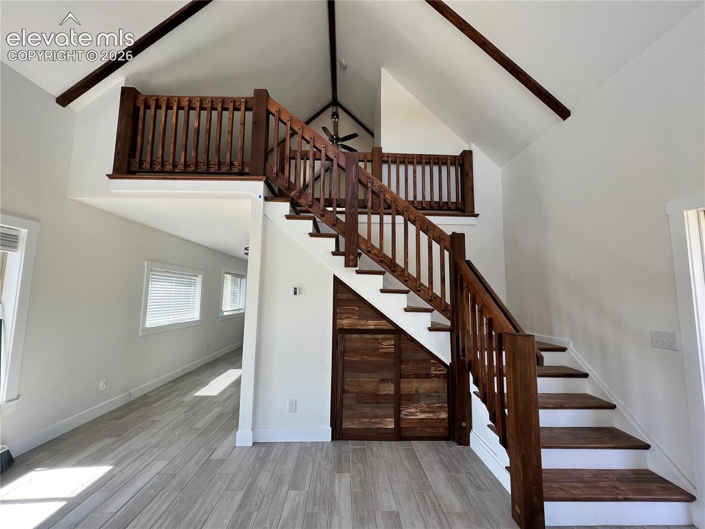 Vaulted ceiling with exposed beams, wood-finish flooring, wood staircase with balusters, wood-paneled wall, and a loft area