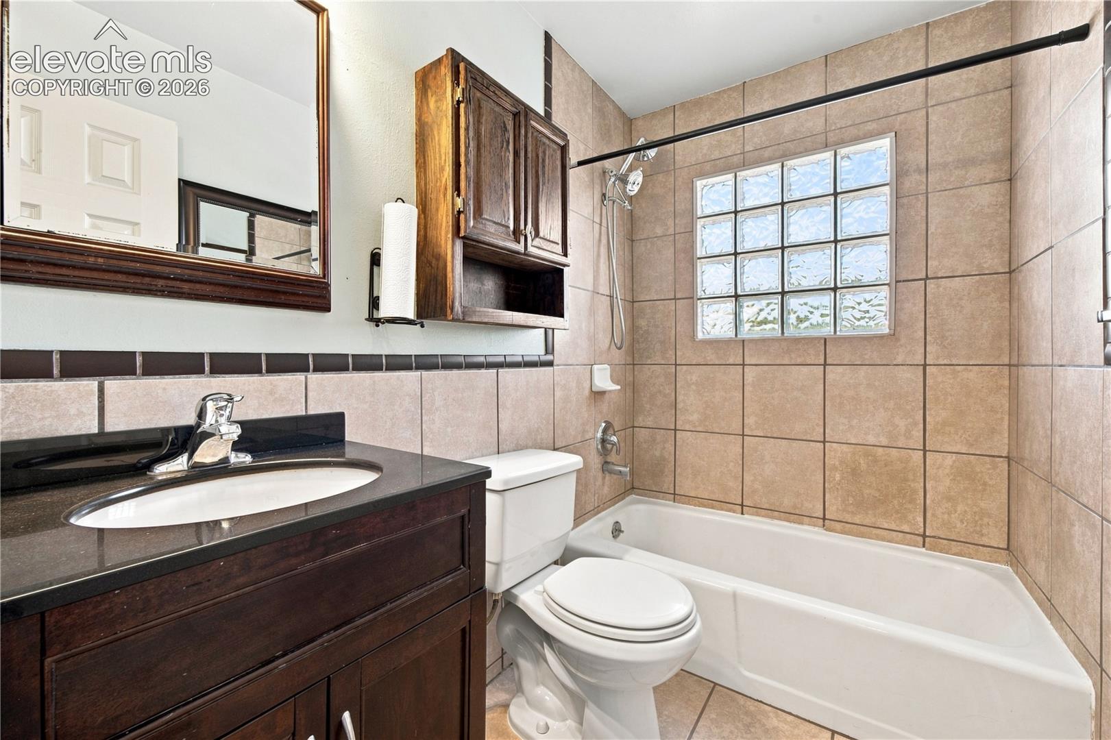 Spa-inspired bathroom featuring a wood-finish vanity with dual sinks, tile surround, and a spacious soaking tub with frameless glass enclosure and tile surround