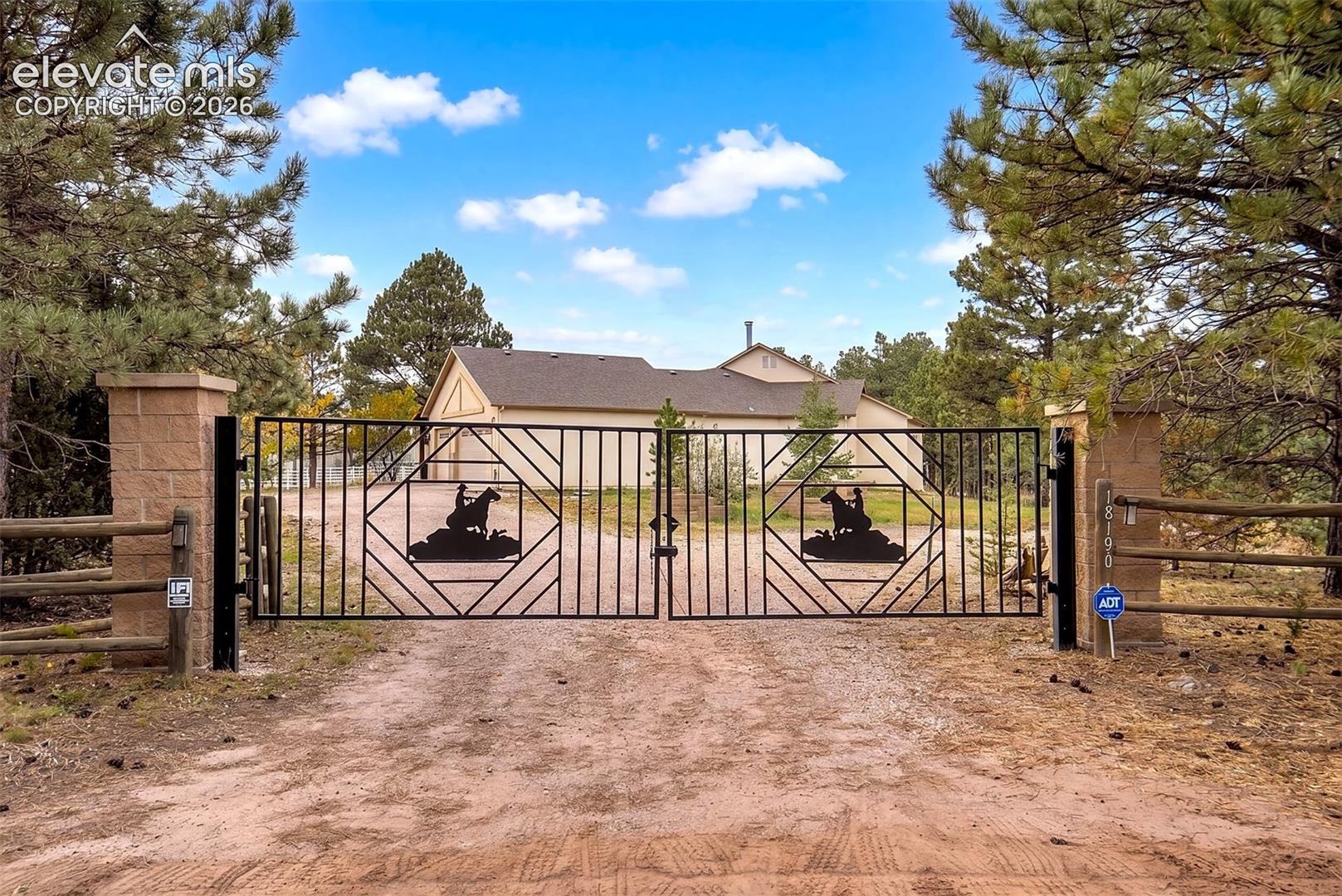 Custom metal entrance gate featuring equestrian-themed silhouettes, dual masonry pillars, and wooden rail fencing