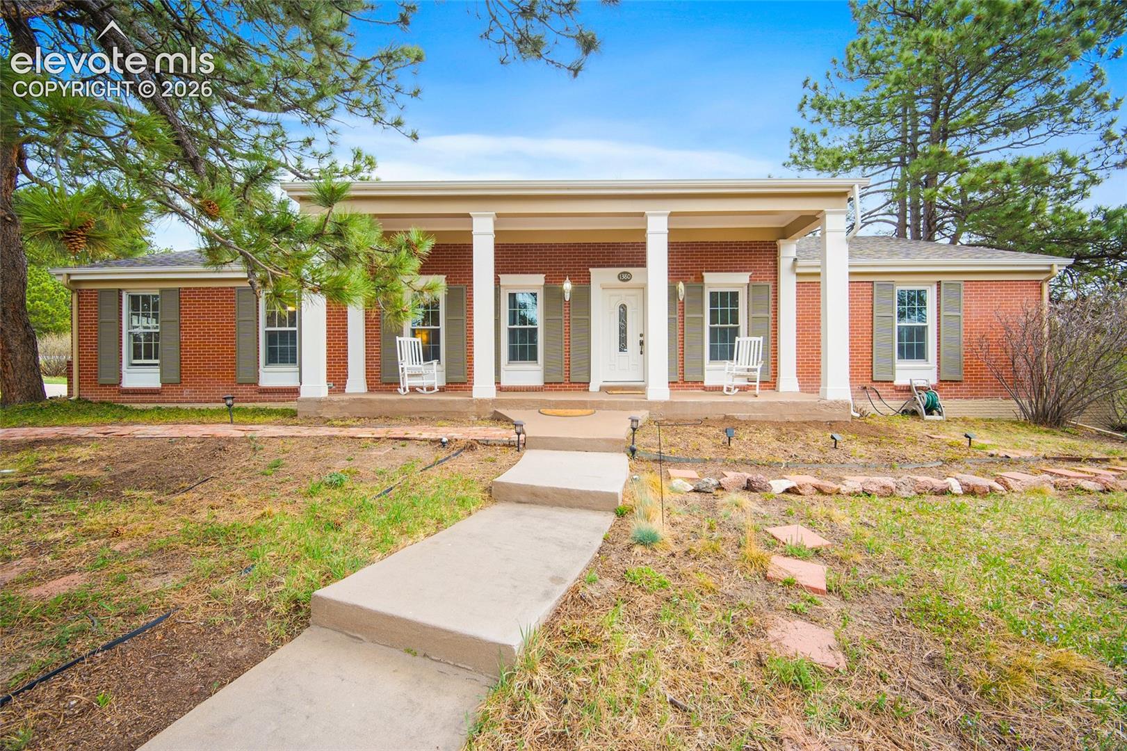 Red brick exterior featuring a covered front porch with structural columns, decorative window shutters, and a concrete walkway