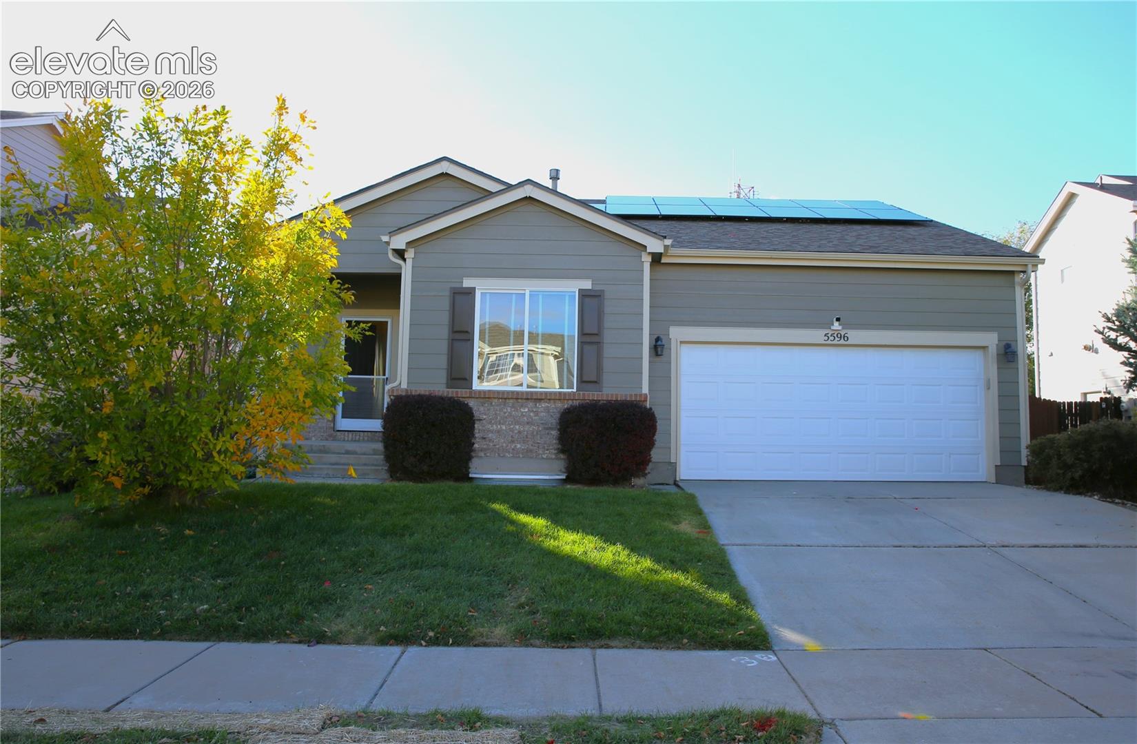Single-story exterior featuring horizontal siding, stone veneer accents, solar panels, attached two-car garage, and concrete driveway