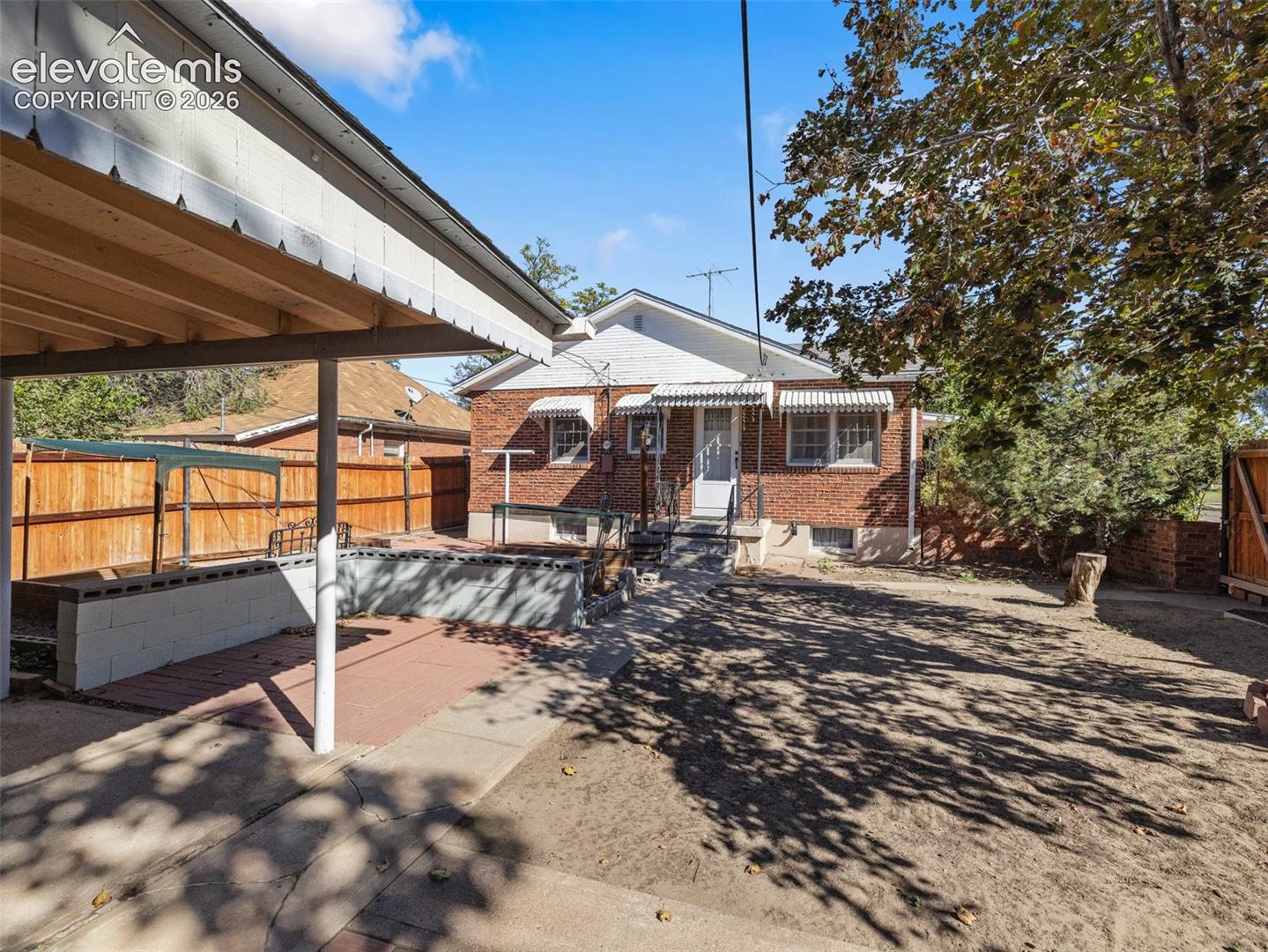 Brick exterior with a covered patio, paved hardscaping, and a fenced yard