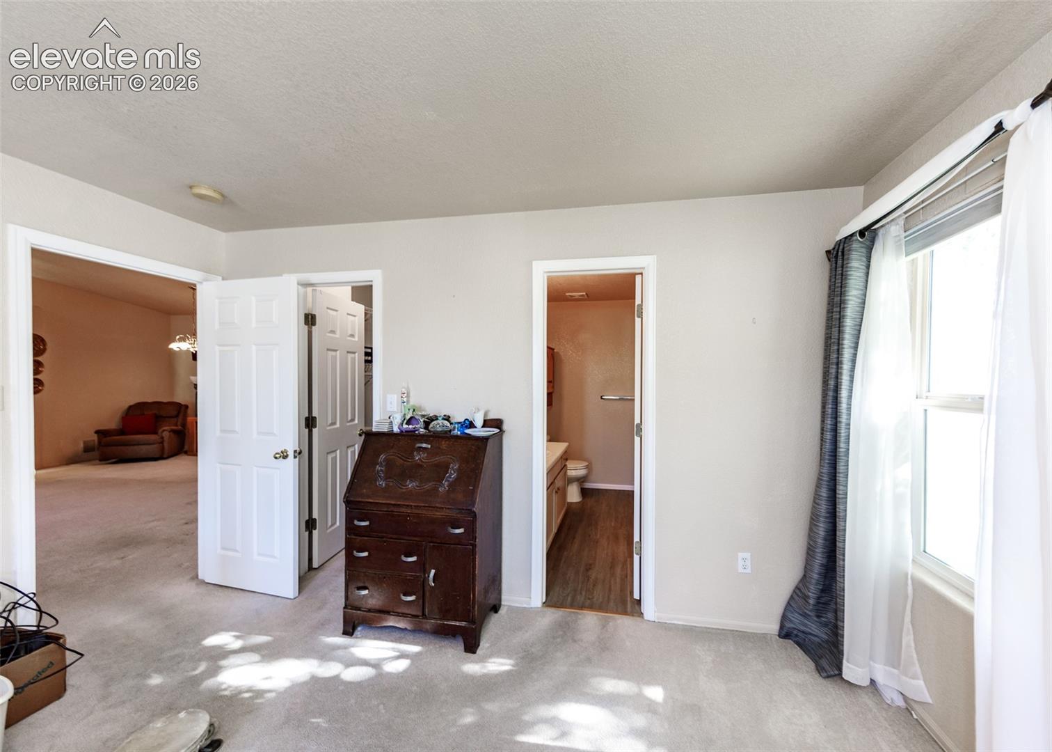 Neutral-toned interior space featuring carpeted flooring, multiple six-panel interior doors, and a window with wood-frame construction