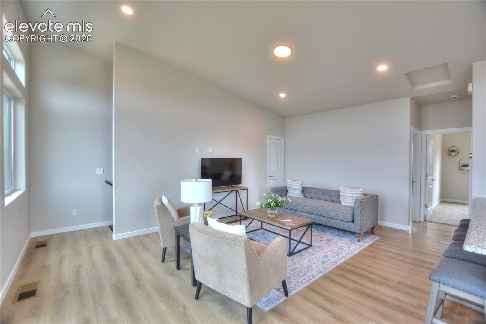 Bright, open-concept living area featuring recessed ceiling lighting, wood-finish flooring throughout, and multiple windows providing natural light