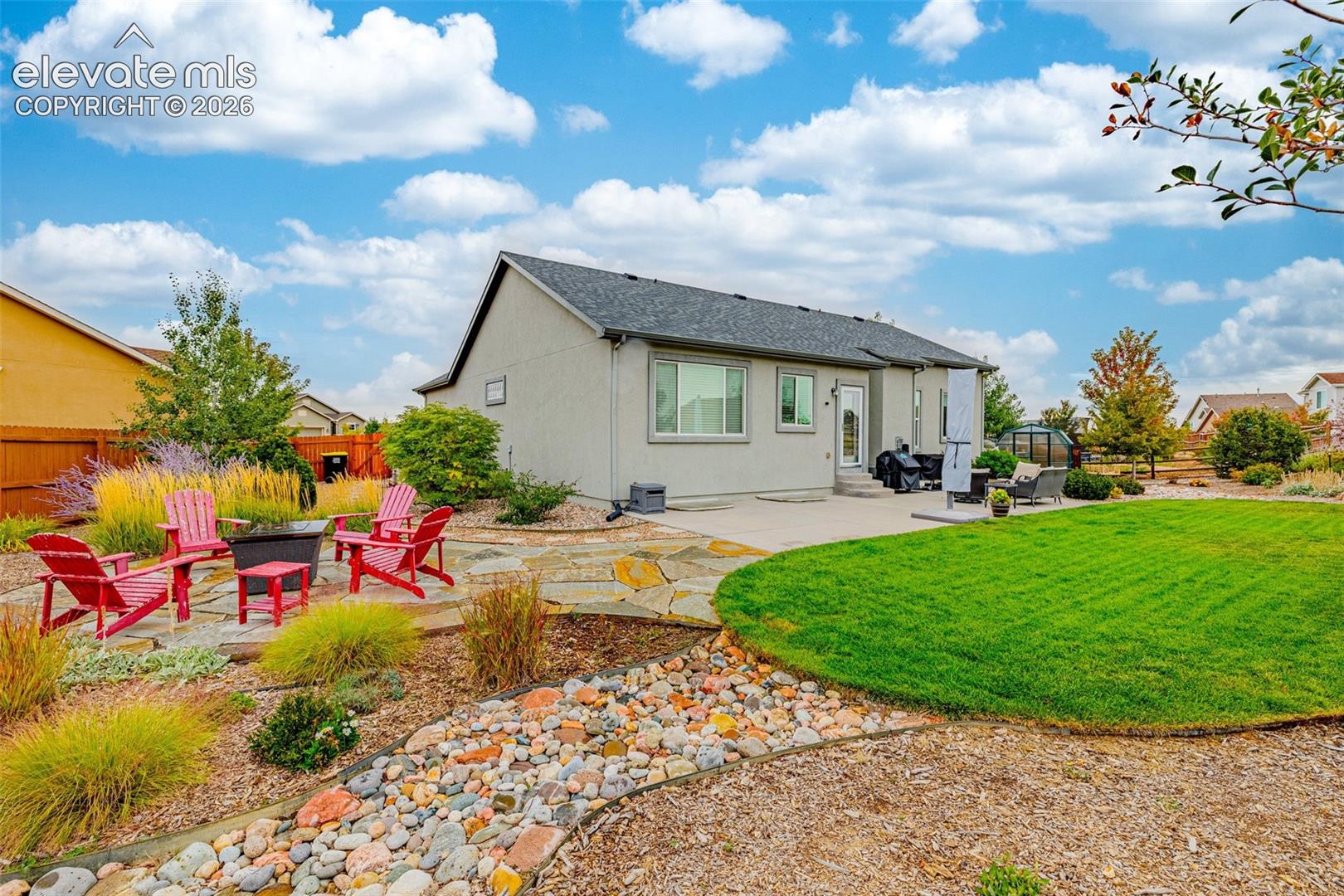 Backyard featuring a concrete patio, irregular flagstone hardscaping, a river rock ground cover border, and a manicured lawn