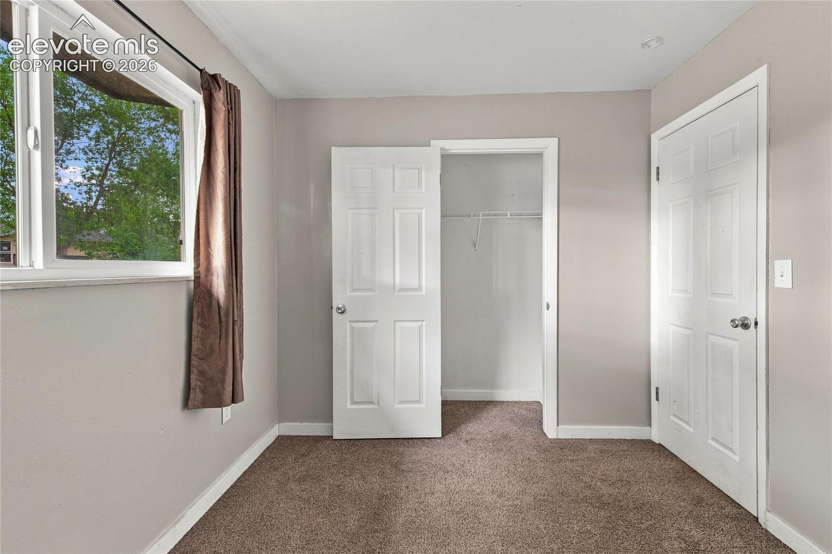 Main level bedroom with large window, carpet and closet space