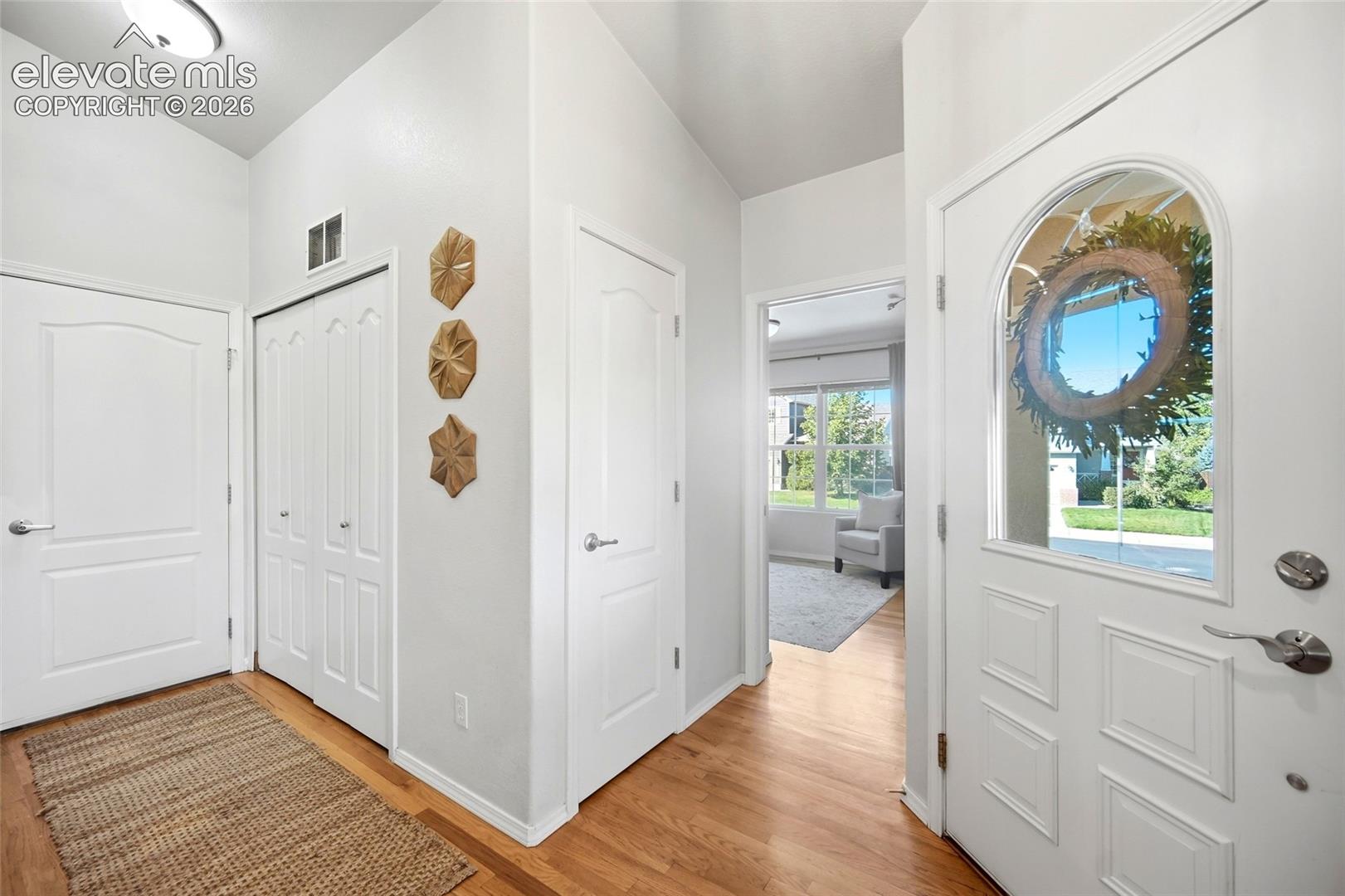 Entryway featuring wood-finish flooring, a paneled door with an arched glass insert, and bi-fold closet doors