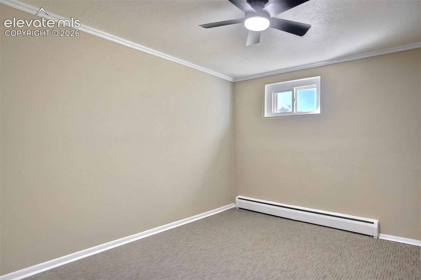 Interior space featuring neutral wall tones, crown molding, patterned carpeted flooring, a ceiling fan with integrated lighting, and a horizontal slider window