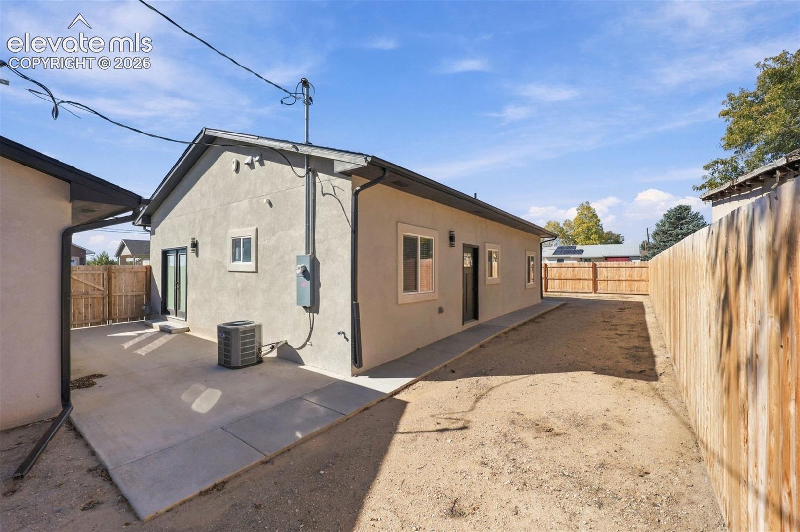 Stucco exterior with multiple windows, concrete patio, and fenced yard