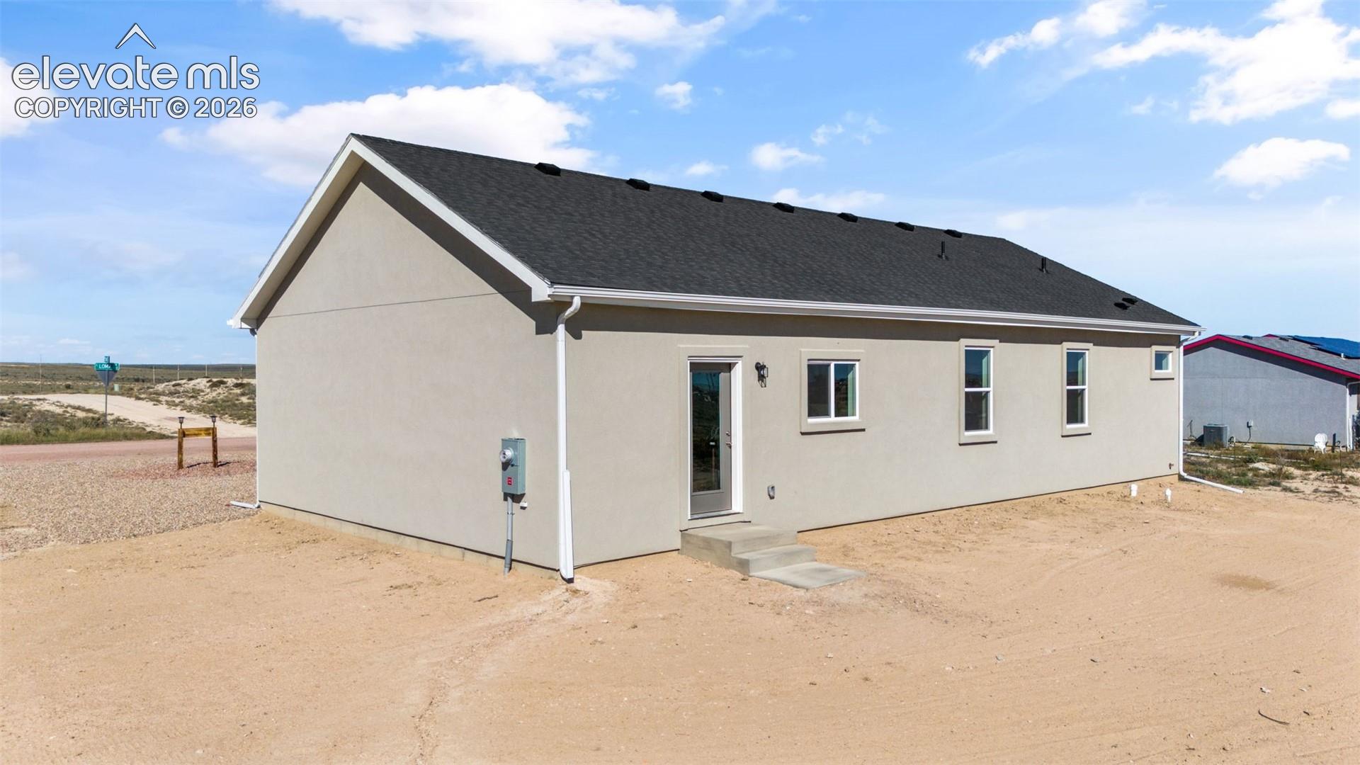 Single-story exterior featuring a light-toned stucco facade, dark shingle roof, white trim accents, and a concrete entry step