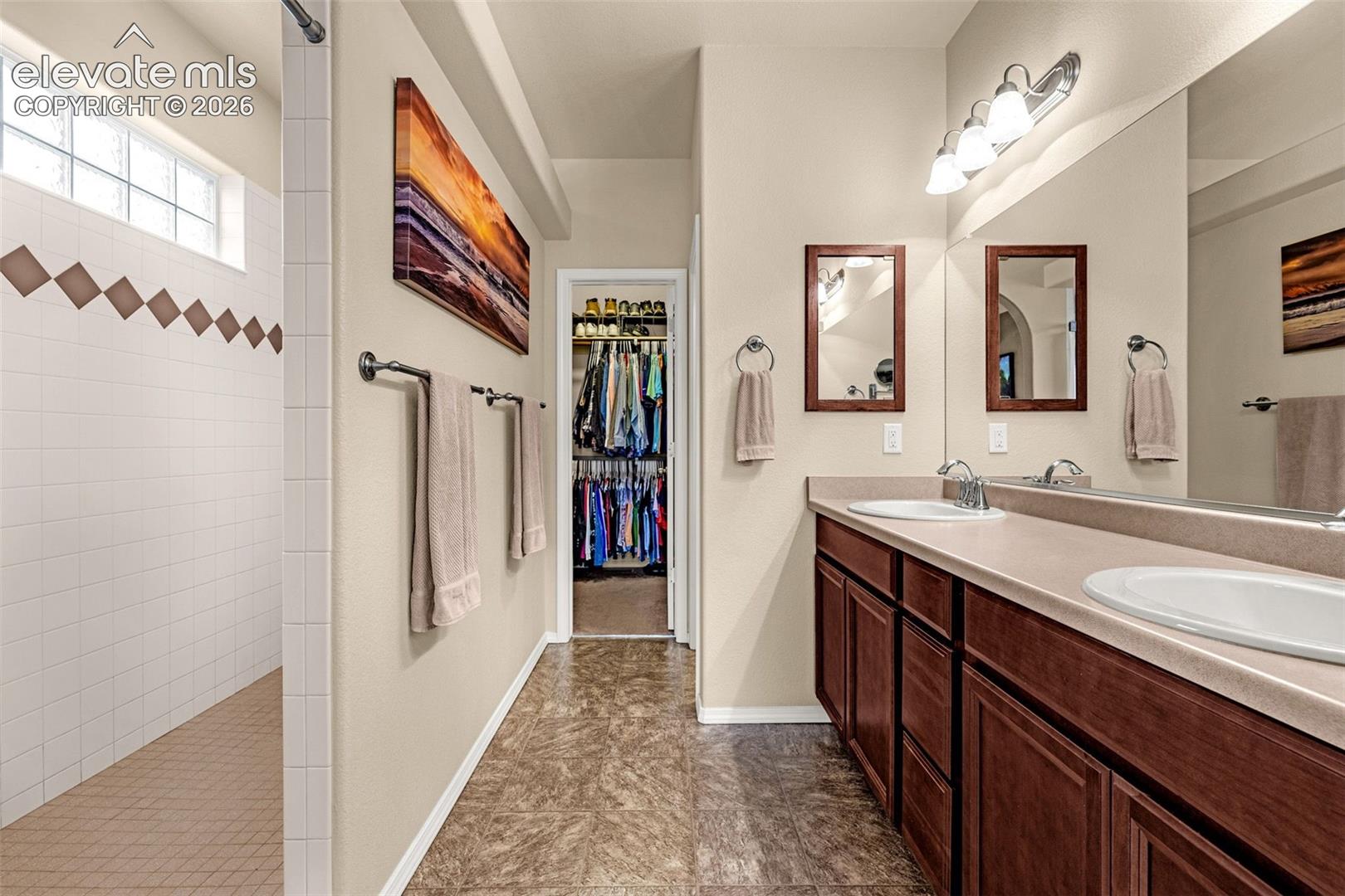 Dual-sink vanity with wood-finish cabinetry, solid surface countertop, inset lighting, and walk-in shower with glass block window
