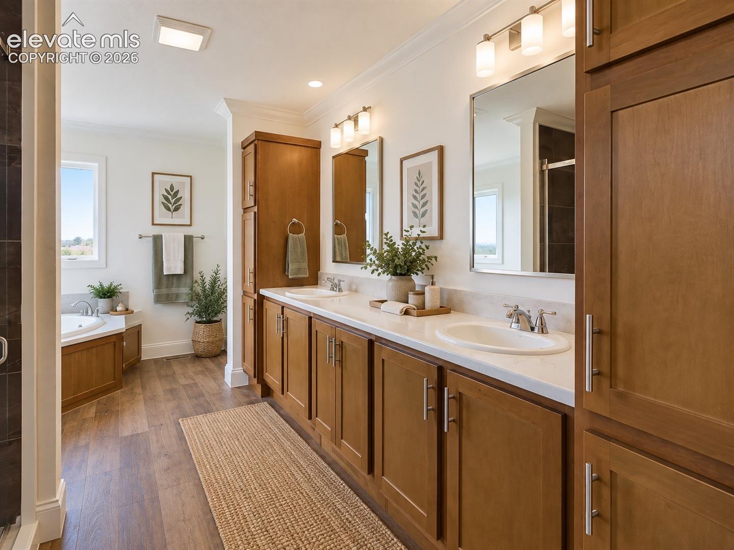 Primary Bathroom – Spacious primary bath features an extended dual-sink vanity with abundant wood cabinetry and storage, complemented by bright vanity lighting and wood-look flooring.