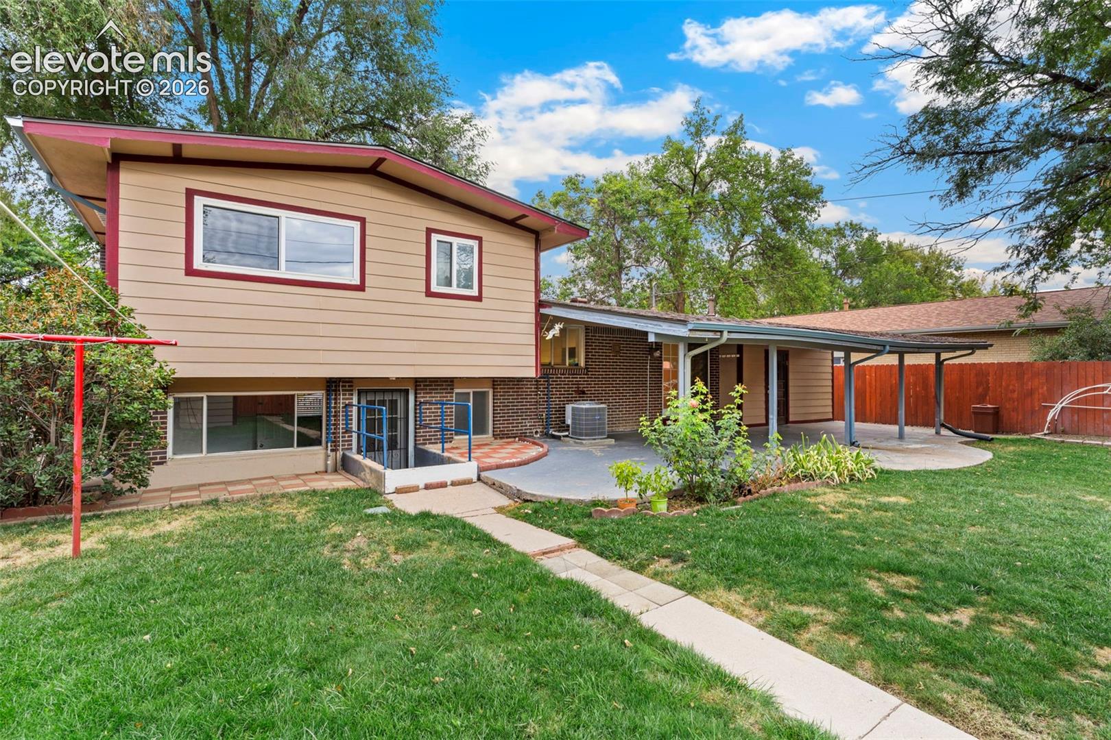Split-level residence featuring a covered patio, extensive lawn, concrete patio, and a privacy fence