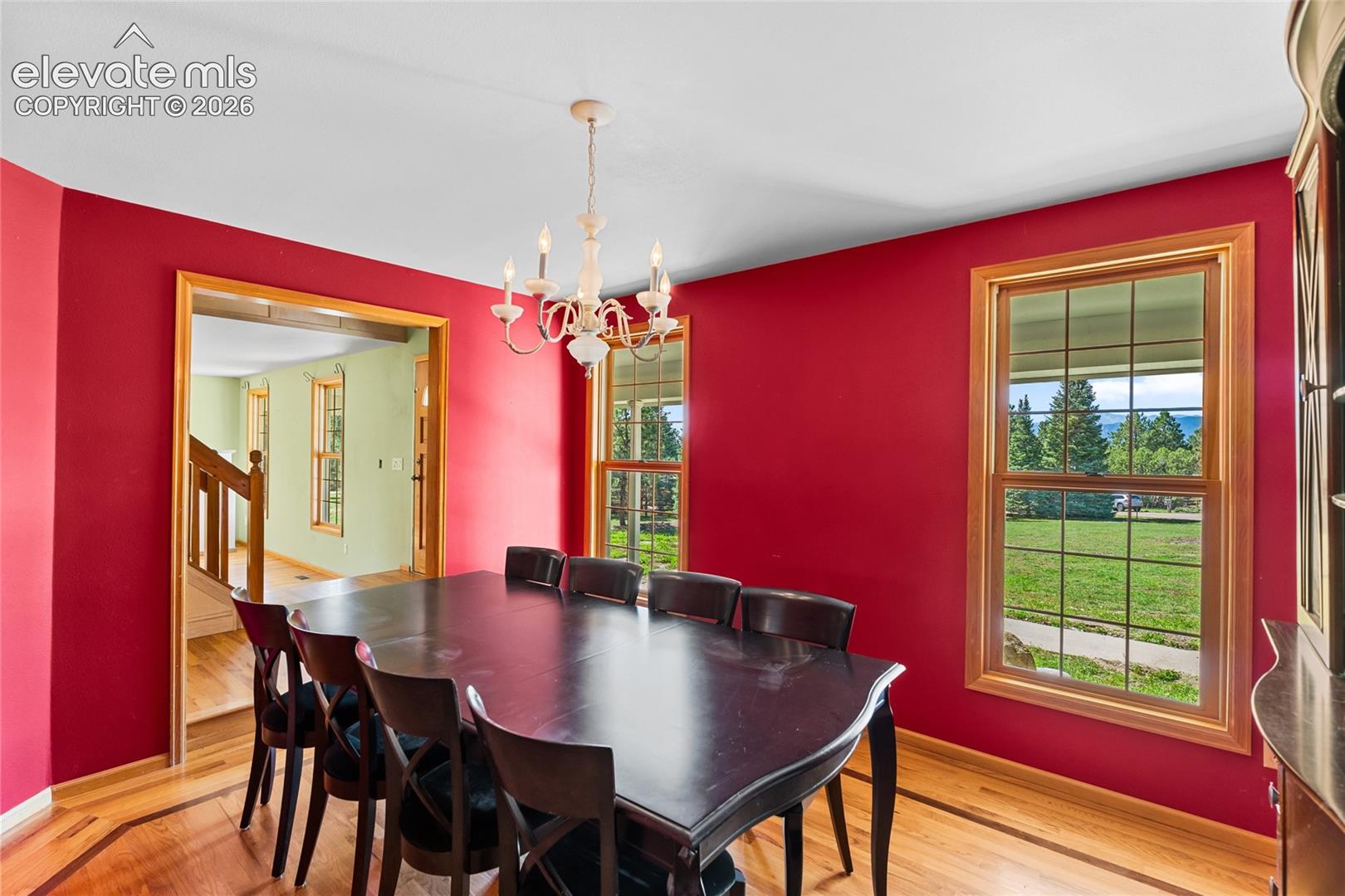 Recessed ceiling with an ornate chandelier, multiple large windows, and wood-finish flooring with border detailing