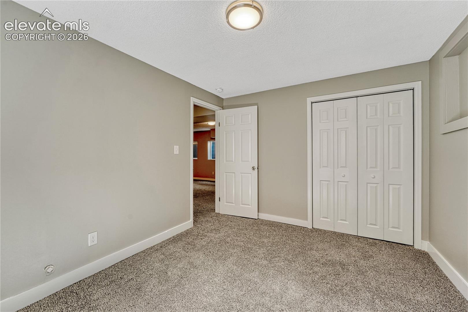 Light gray wall paint, textured ceiling, flush mount ceiling light fixture, white interior door, and bi-fold closet doors