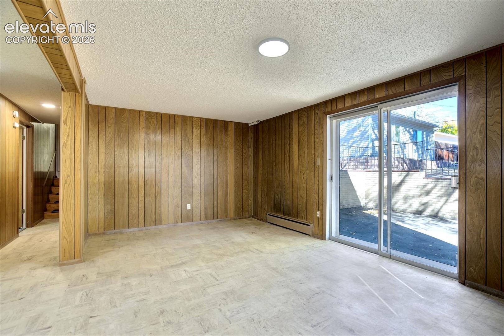 Interior room featuring floor-to-ceiling wood paneling, sliding glass patio door, and tile flooring