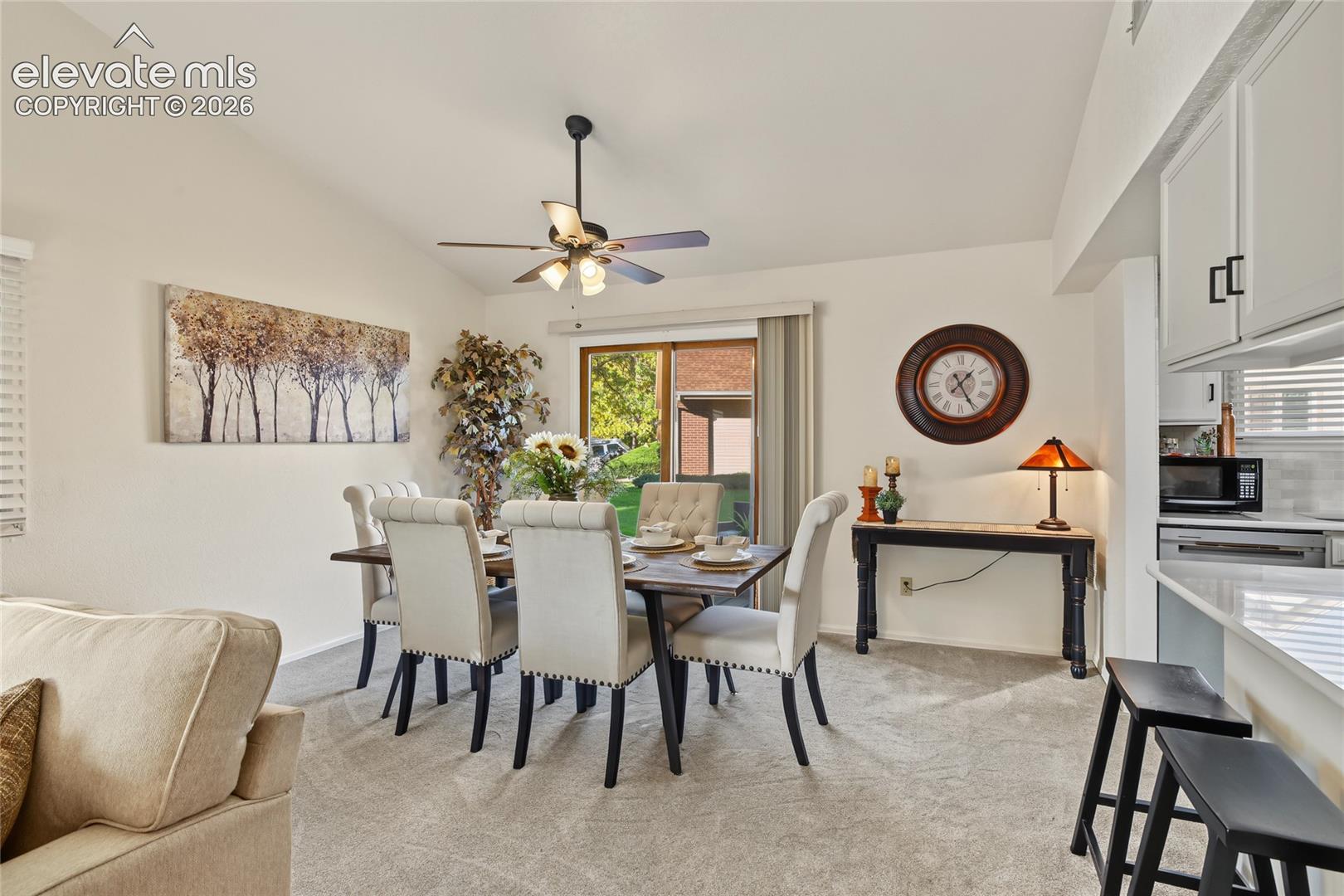 Vaulted ceiling, ceiling fan, sliding glass door, carpet flooring, white cabinetry