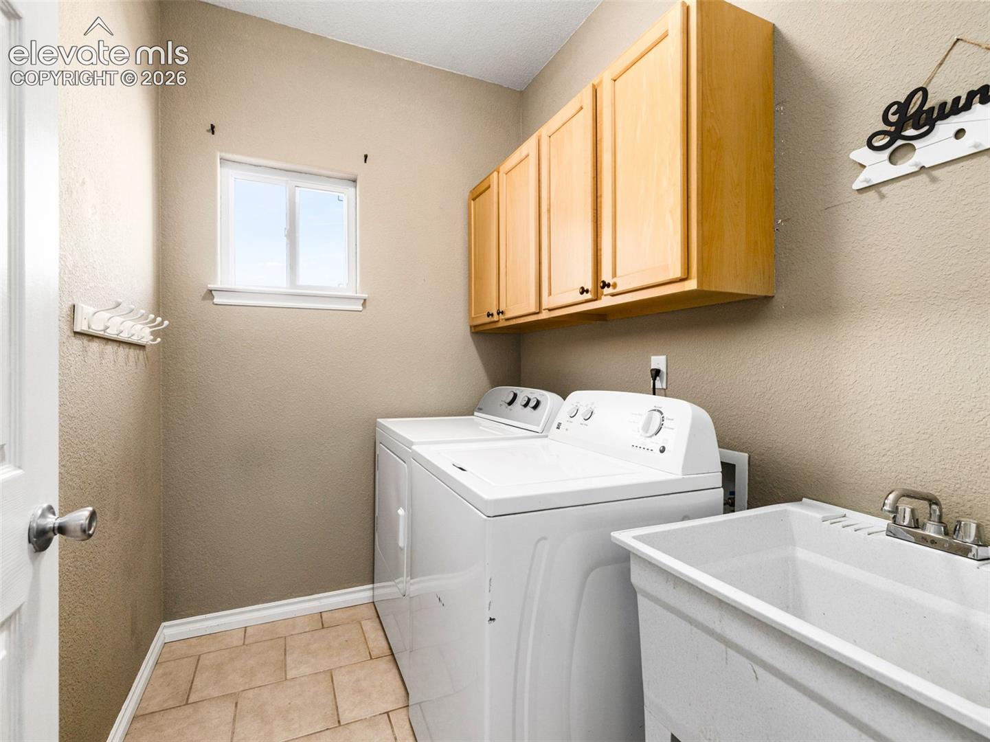 Laundry room featuring light wood cabinetry, a utility sink, and tile flooring