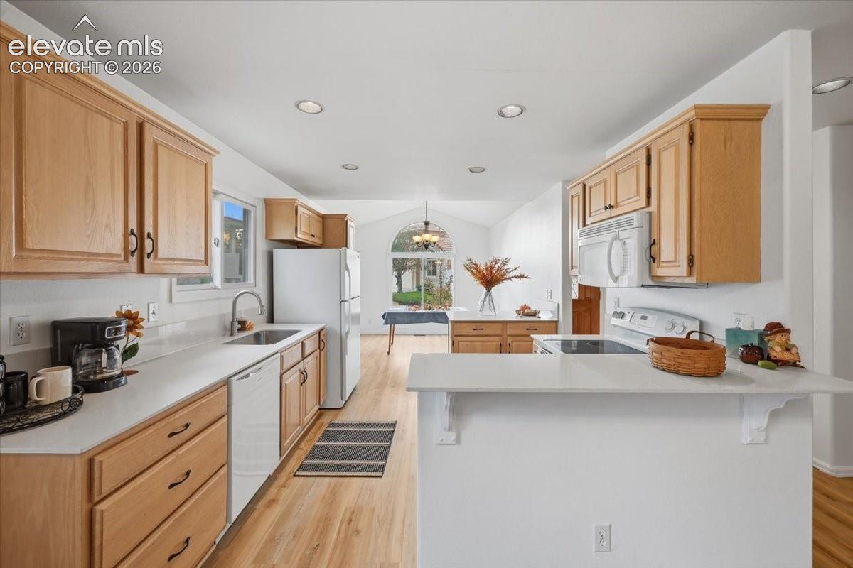 Kitchen featuring wood cabinetry, light-toned countertops, wood-finish flooring, recessed lighting, and a breakfast bar