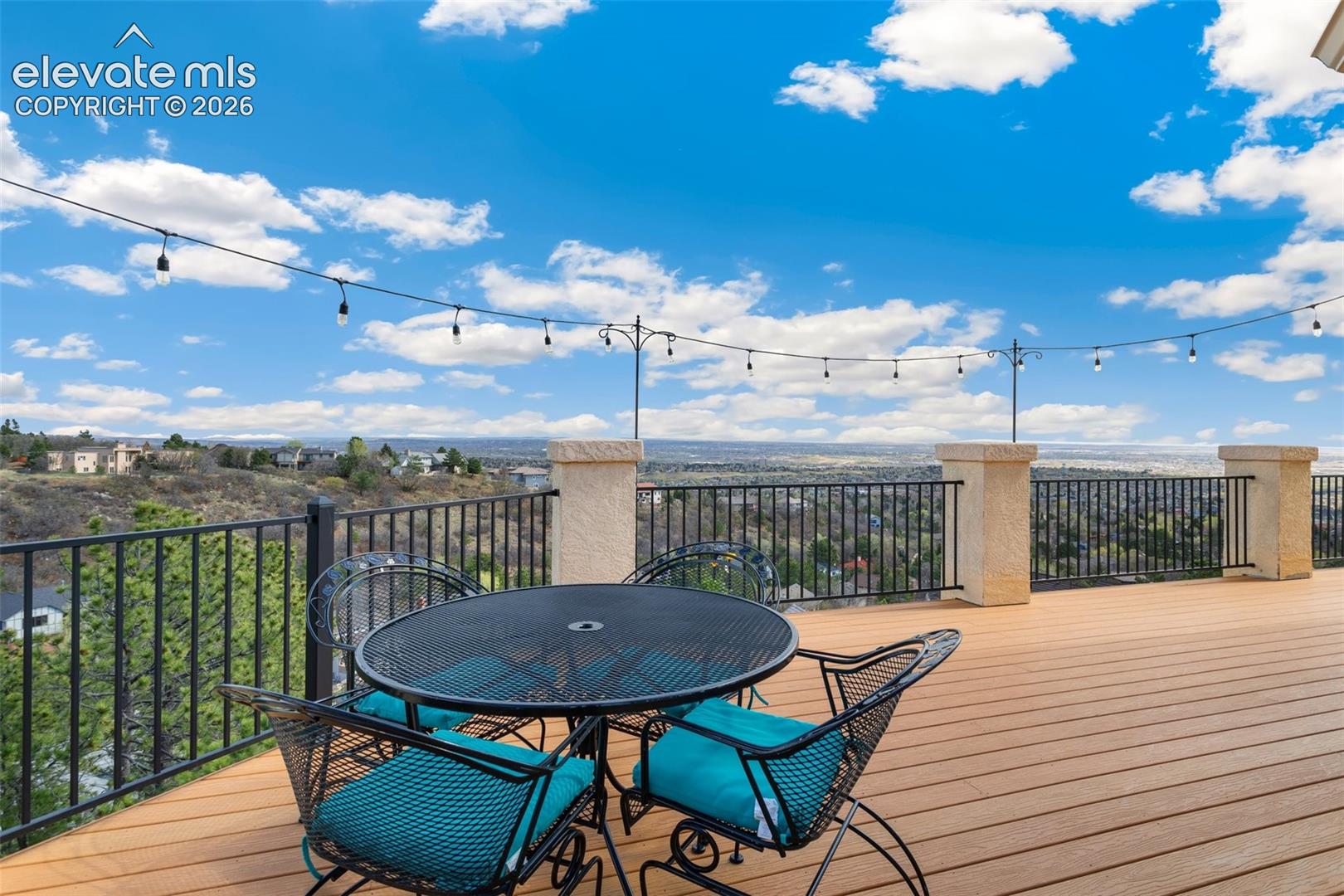 Expansive outdoor deck featuring wood-finish decking, decorative string lighting, and wrought iron railings with substantial stone pillars