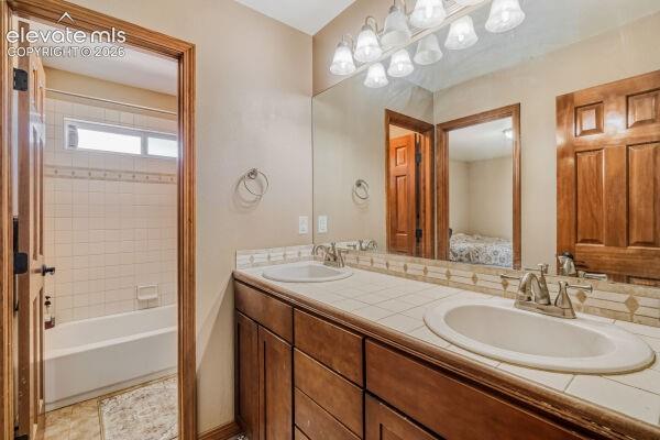 Bathroom featuring a dual vanity with tile countertop, wood cabinetry, and an overhead vanity light fixture